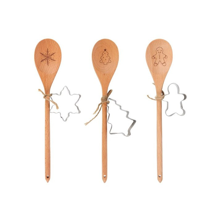 Three wooden spoons with festive designs—a snowflake, Christmas tree, and gingerbread person—each tied with twine and paired with a metal biscuit cutter, perfect for whipping up seasonal treats and puddings.