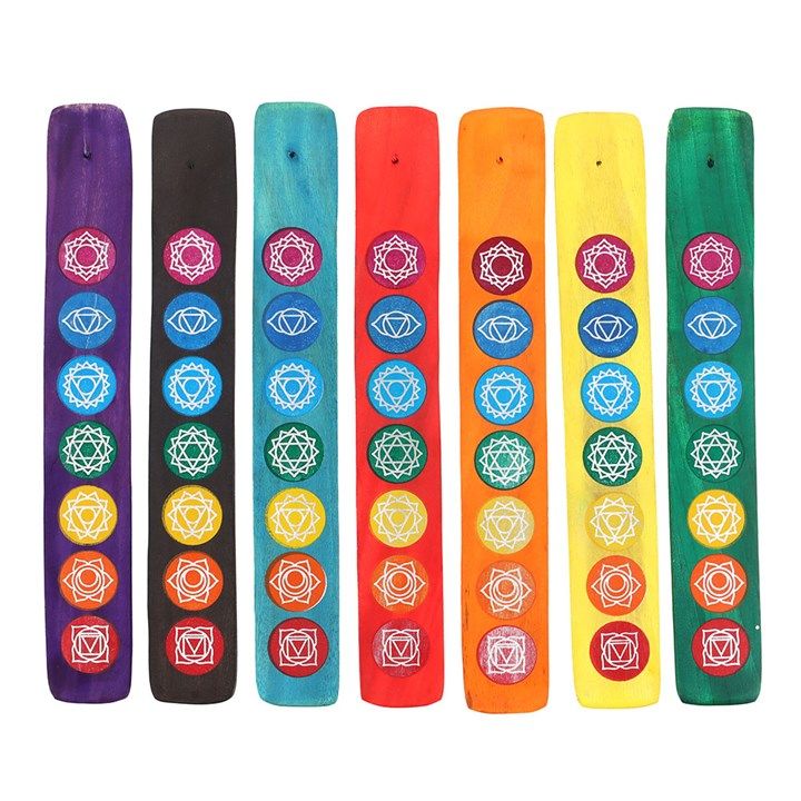 Seven vibrant chakra incense holders are arranged in a row, each painted in colours corresponding to the energy centres: purple, blue, light blue, green, yellow, orange, and red. Adorned with white chakra symbols, they feature larger circles at the base and smaller ones above—perfect for meditation.