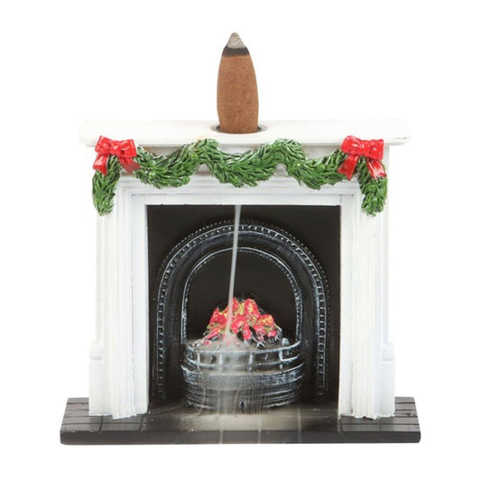 A miniature Christmas fireplace adorned with festive garlands and red bows burns a backflow incense cone, sending smoke down into the painted fire and hearth for a realistic chimney effect.