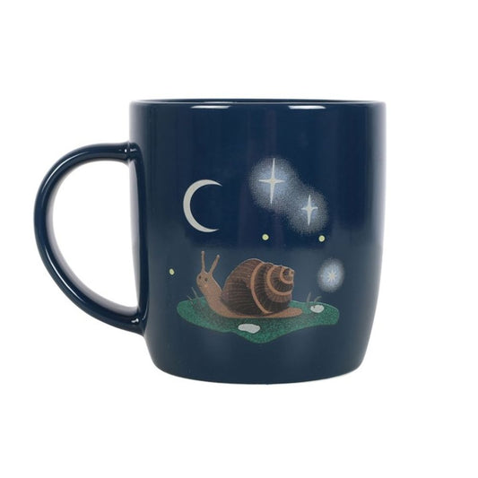 A navy-blue mug features a whimsical illustration of a snail on grass beneath a crescent moon, surrounded by sparkling stars and glowing orbs. The mugs large handle is conveniently positioned on the left side, adding to its charm.