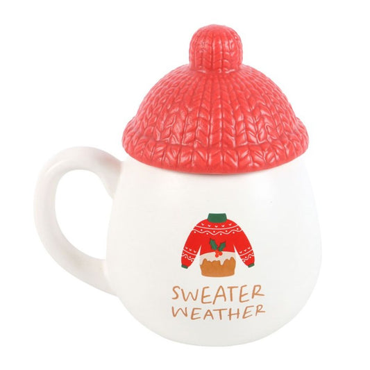 A novelty mug with a handle and a red lid shaped like a knitted beanie. This Sweater Weather mug features an illustration of a red jumper and the words “SWEATER WEATHER”—perfect for Christmas cosiness.