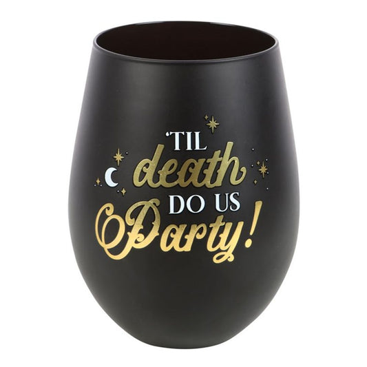 A black and gold stemless wine glass with a matte finish, featuring gold and white lettering: “‘TIL death DO US Party!” It is decorated with a skeleton design, small stars, dots, and a crescent moon on its rounded shape.