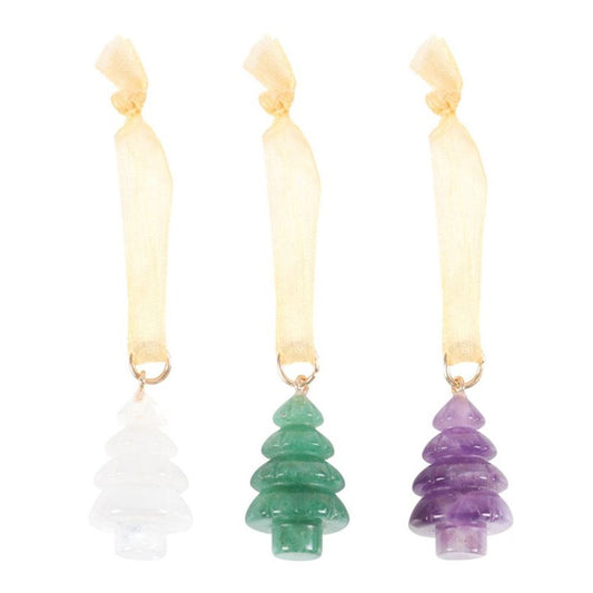 Three gemstone tree decorations—white, green, and purple—hang from sheer gold ribbons tied in loops. Each decoration is carved to resemble a stylised pine tree, bringing crystal elegance to any festive décor. The background is plain white.