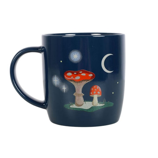 A navy-blue mug decorated with magical toadstools featuring red caps and white spots on a lush patch of grass. White stars and a crescent moon illuminate the sky, creating a whimsical, night-time scene.