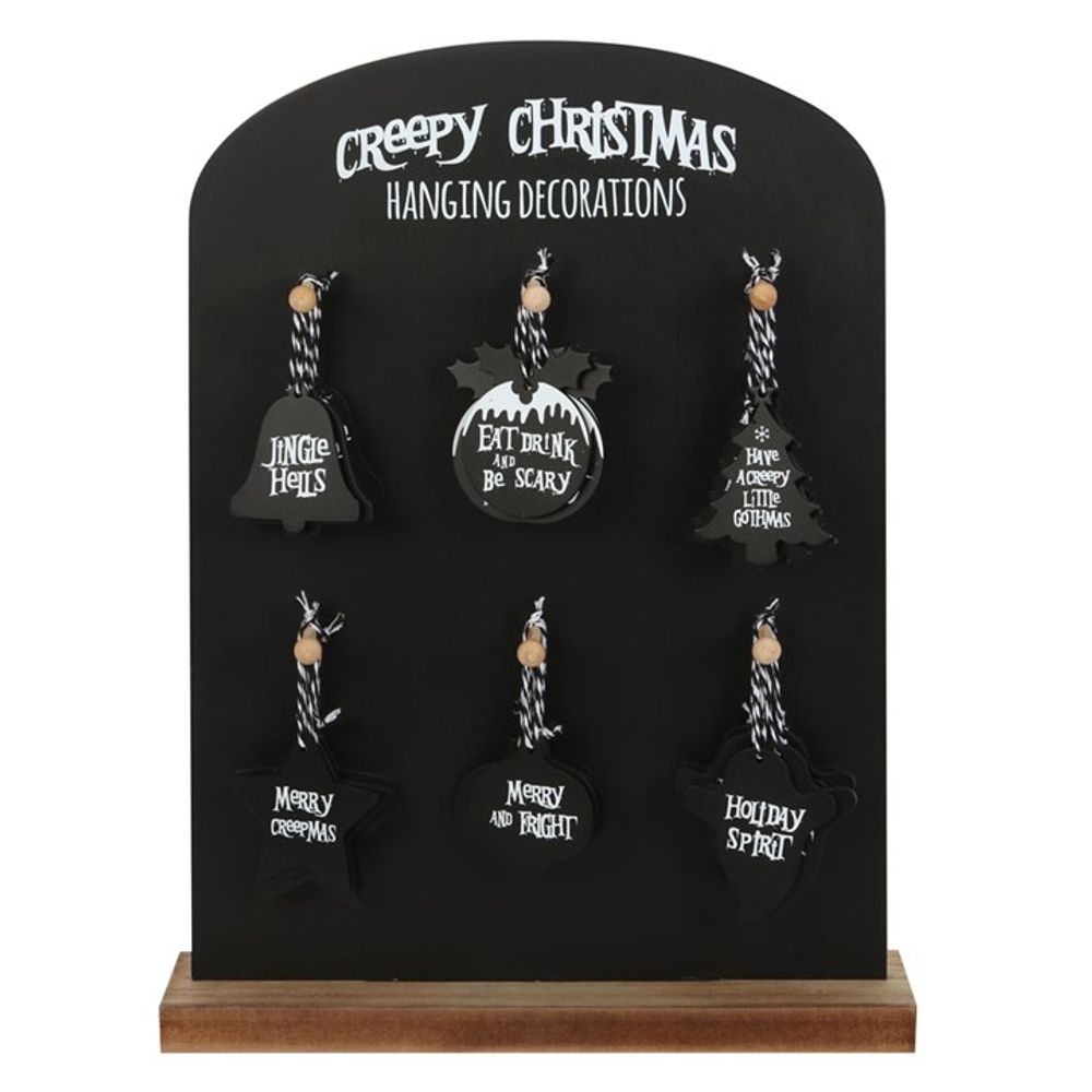 A black display board labelled Creepy Christmas Hanging Decorations showcases six gothic ornaments featuring spooky festive phrases—perfect for alternative retail shops. Each ornament hangs from twine and is shaped like a bell, a star, or a bat.