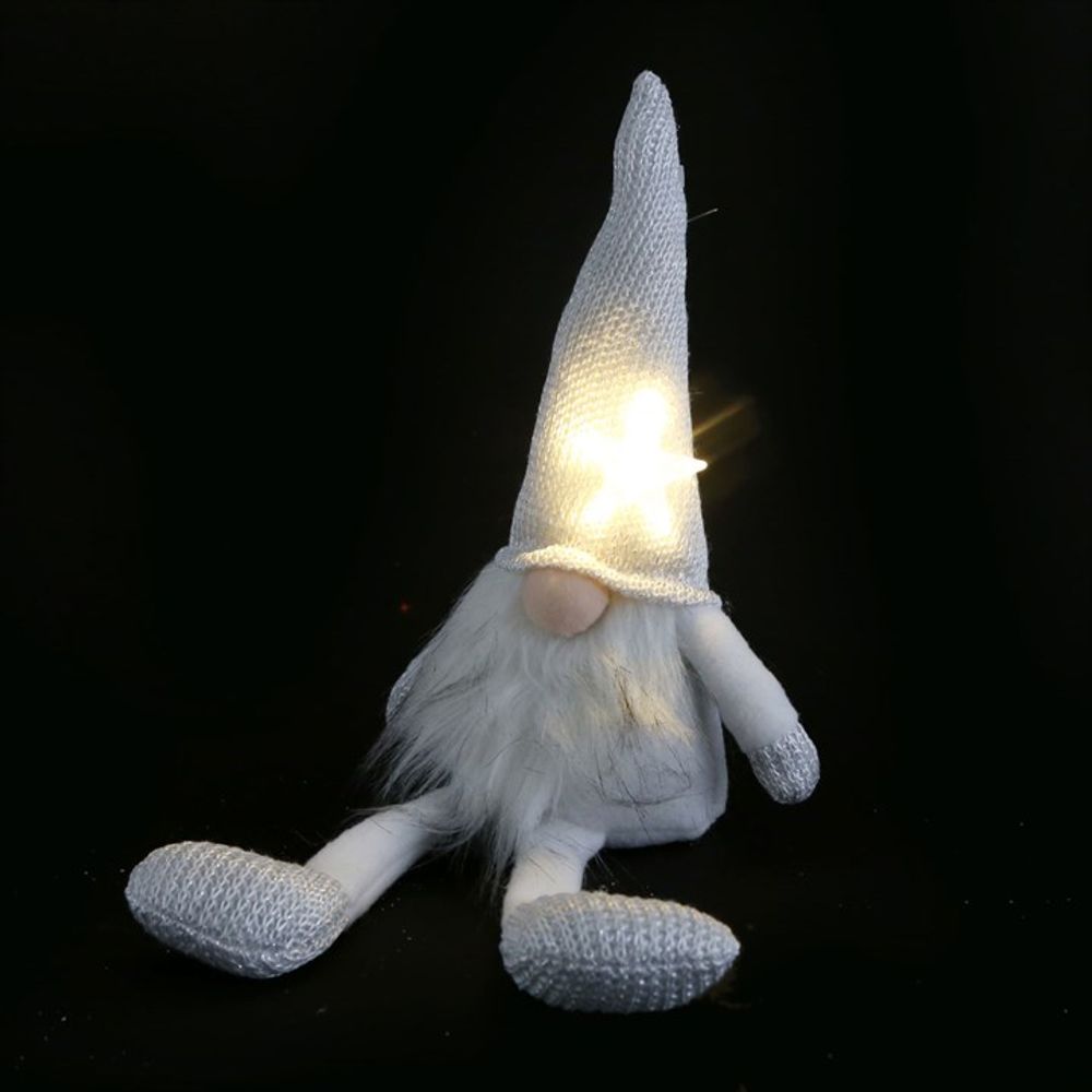 A soft, white and silver plush Santa gonk sits against a black background. Its tall, glowing hat with a star cut-out brings festive cheer, partially covering the gnome’s round nose and long white beard.