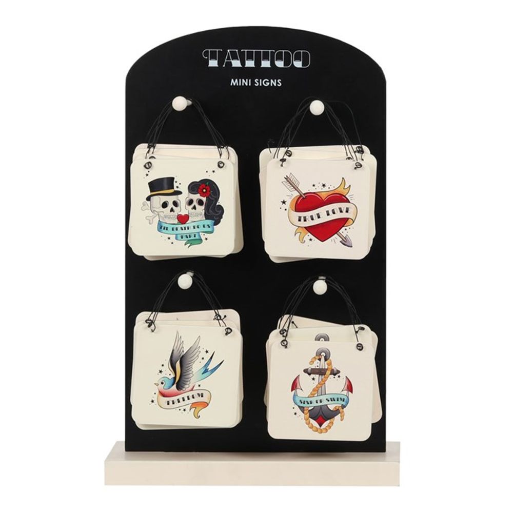 A black display stand labelled TATTOO MINI SIGNS holds four quirky miniature hanging signs with vintage tattoo designs—a skull, heart, bird, and anchor—each suspended by black string for a subtle gothic twist.