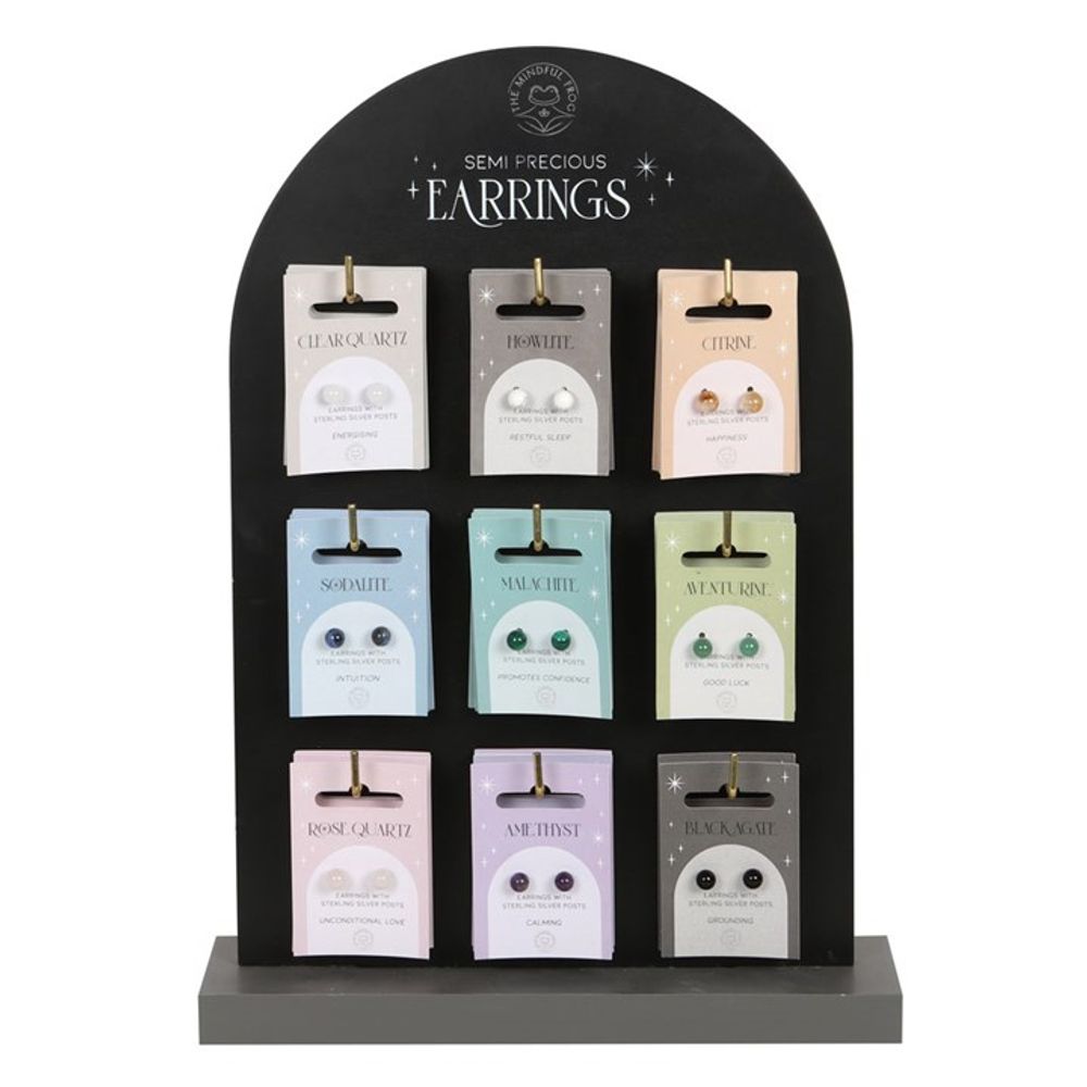 A black display stand holds nine pairs of crystal stud earrings on pastel-coloured cards, each labelled with a semi-precious stone and its spiritual meanings. The header reads “Semi-Precious Earrings.”.
