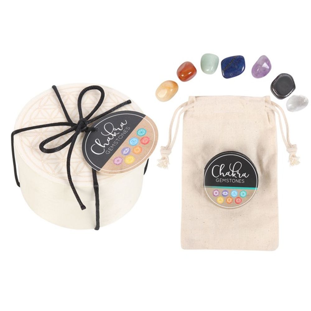 Gift set with chakra gemstones and a pouch. The round box, adorned with a black bow and label, contains colourful stones, each designed to balance chakras. The beige pouch also has a label. The stones are red, orange, yellow, green, blue, purple, and black in colour.
