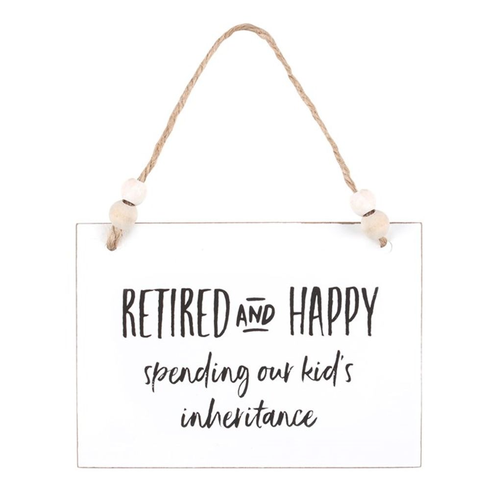 A charming wooden hanging sign with black text hangs by a twine string adorned with white beads. The text humorously proclaims, RETIRED AND HAPPY spending our kids inheritance. Its simple design and casual, handwritten-style typography make it a delightful present.