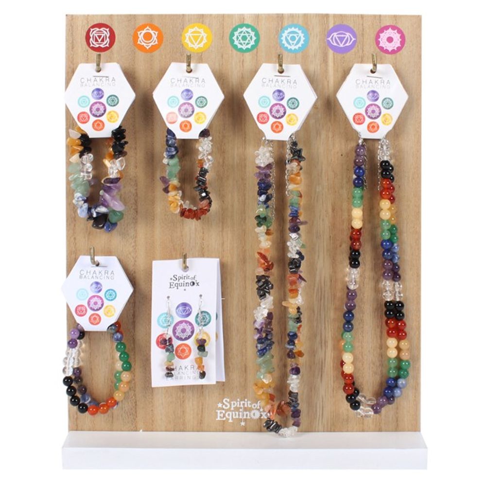 A wooden display stand holds colourful chakra jewellery—bracelets, stone chip bracelets, beaded necklaces, and chakra earrings—each labelled with chakra symbols and “Chakra” tags. A “The Spirit of Equinox” card is also present.