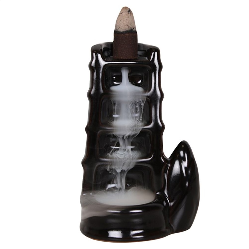 Ceramic backflow incense burner shaped like a black bamboo shoot with an incense cone on top. White smoke cascades in a waterfall effect down steps inside, collecting at the bottom. The surface is glossy and smooth.