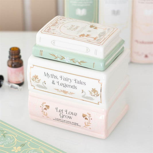 Three ceramic containers shaped like a stack of pastel books, each featuring decorative titles. A small brown dropper bottle rests nearby, ideal for use as a fragrance oil diffuser or ceramic oil burner.