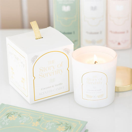 A white coconut and vanilla candle labelled The Story of Serenity burns beside its matching box—an inviting home fragrance and the perfect gift for book lovers. Soft pastel packaging and green envelopes are blurred in the background.