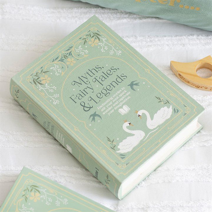A pastel green hardback book titled “Myths, Fairy Tales, & Legends”, ideal for vintage book storage or as a charming bookshelf storage solution, features two white swans and floral designs on the cover, resting on textured white fabric.