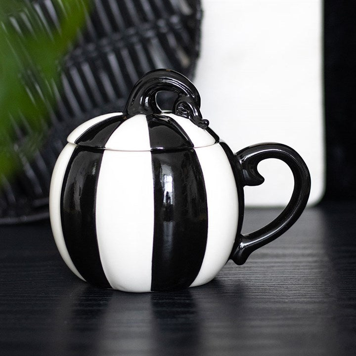 A black and white striped mug with a lid, featuring ornate curved details on the handle and lid. Perfect for a spooky mug collection, it sits on a dark surface with a blurred monochrome background.