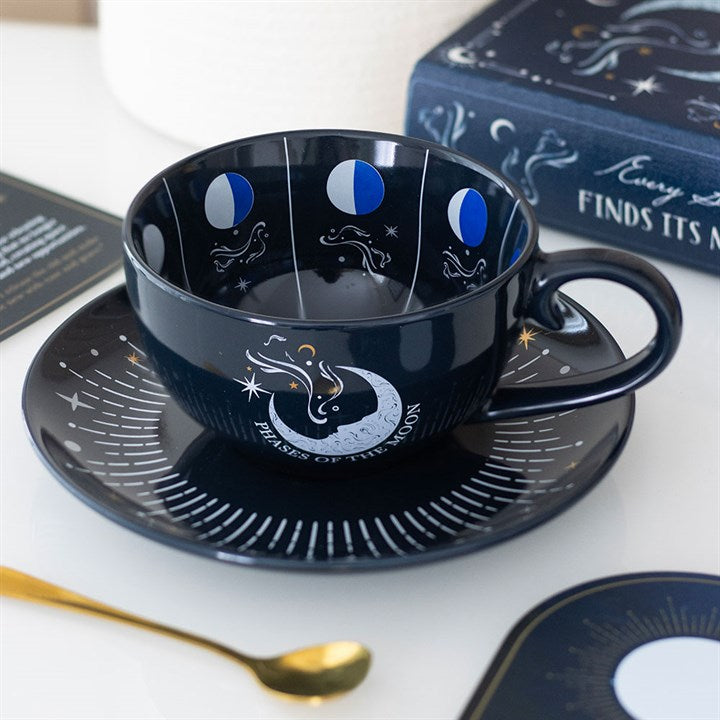 A dark blue moon phase teacup and saucer set, decorated with white and gold lunar phases and stars—ideal for celestial tea rituals. Inside, illustrations encourage tea leaf reading. Comes with a gold spoon and book.