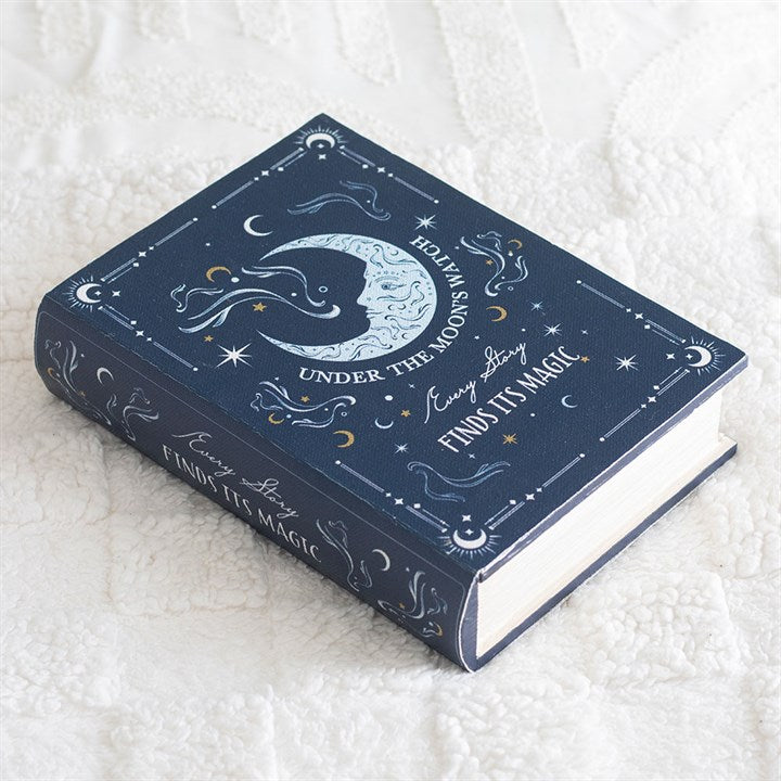A navy blue secret storage box adorned with celestial illustrations—moon, stars, clouds—rests on a white textured surface. The lid features the words “Follow the moon & stars…every story finds its magic” in decorative script.
