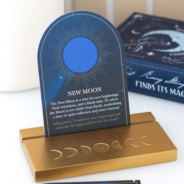 A gold stand displays a moon phase card showing a blue new moon against a starry night. This spiritual gift emphasises the new moon as a time for fresh starts and features an uplifting affirmation.