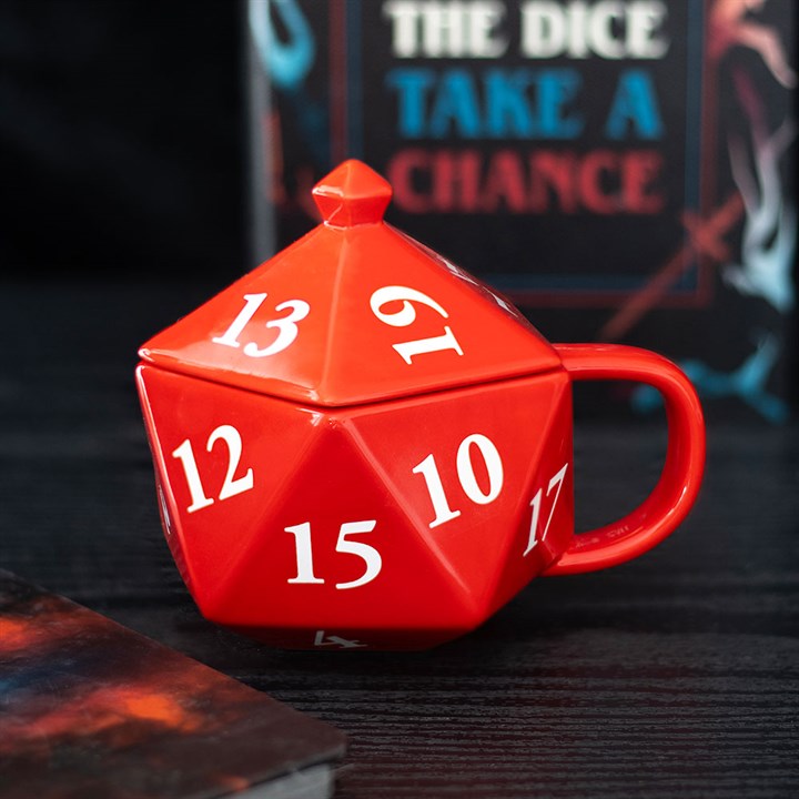 A red D20 mug, shaped like a twenty-sided die, sits on a dark surface; its white numbers and matching lid ready for your next adventure. In the background, a book titled “THE DICE TAKE A CHANCE” is partially visible.