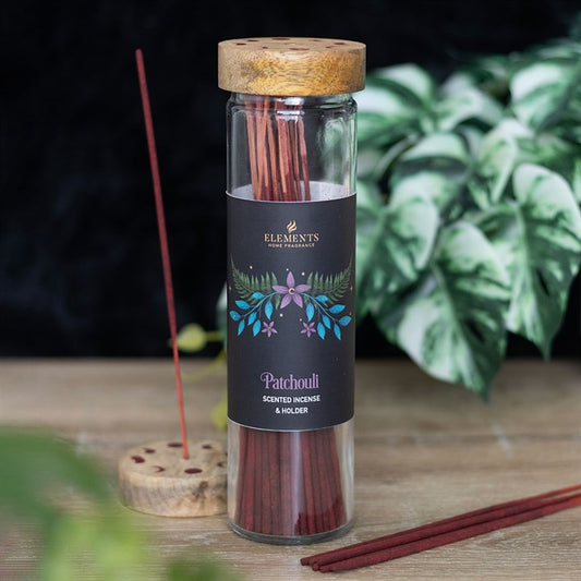 A glass jar with a wooden lid contains red incense sticks labelled Patchouli Scented Incense & Holder. One stick burns in a wooden holder nearby, filling the tranquil space with the scent of patchouli; green plants are softly blurred in the background.