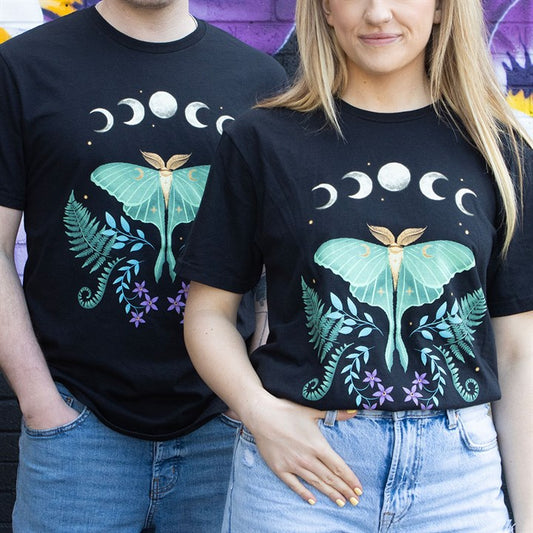 Two people stand side by side in unisex black T-shirts featuring a large green luna moth, ferns, purple flowers, and moon phases. Their torsos are visible in front of a colourful graffiti wall.