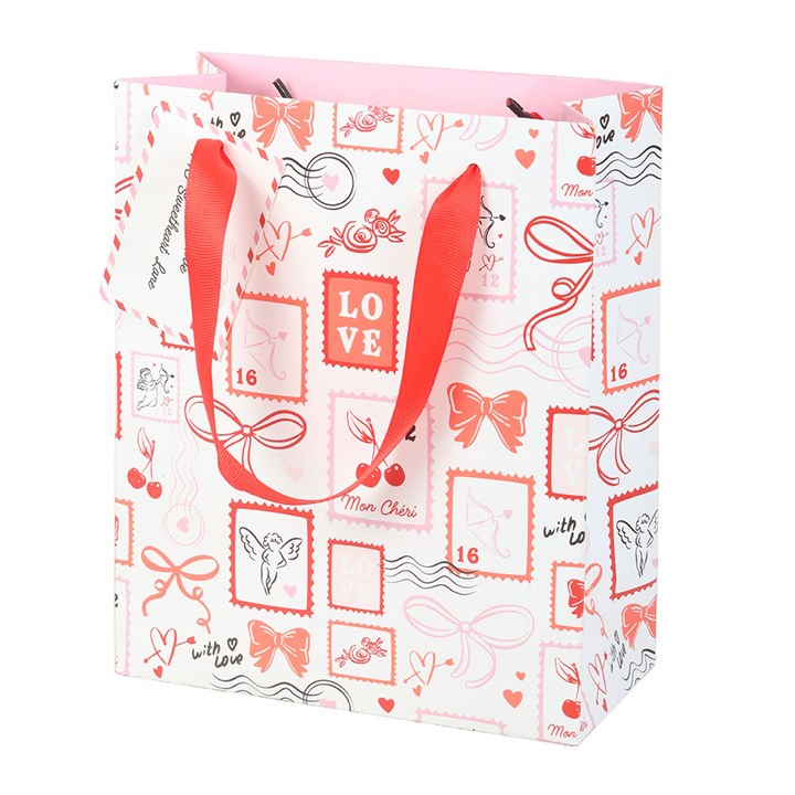 A white Valentine’s Day gift bag decorated with red and pink LOVE-themed designs—bows, hearts, and stamps. It has red ribbon handles, a matching gift tag, and a pale pink interior.