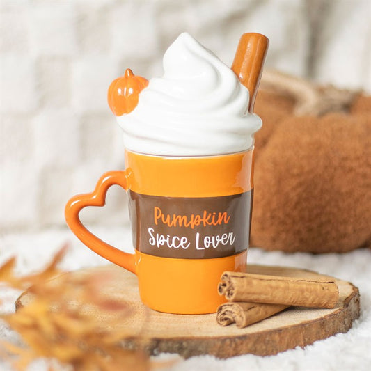 An orange ceramic mug with a lid and a heart-shaped handle, labelled “Pumpkin Spice Lover”, is topped with whipped cream, a cinnamon stick, and a pumpkin decoration—an essential for coffee lovers and fans of pumpkin spice lattes.