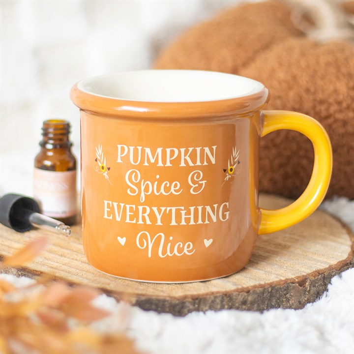 A brown mug with a yellow handle sits on a wooden coaster. Nearby, an autumn-themed wax melt adds to the cosy scene. The mug reads Pumpkin Spice & Everything Nice in white letters, with small decorative leaves.