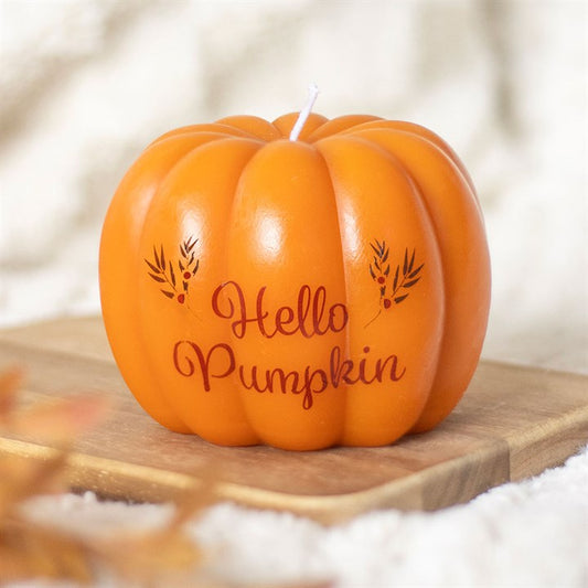 An orange, pumpkin-shaped candle with “Hello Pumpkin” and small leaf designs sits on a wooden tray against a soft, neutral background—a perfect cosy gift for autumn décor enthusiasts.