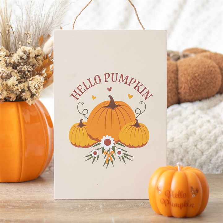 A rectangular Halloween sign featuring a charming pumpkin design reads HELLO PUMPKIN, surrounded by flowers and leaves. A pumpkin vase with dried blooms and an autumn decorative candle add warmth to the cosy décor in the background.