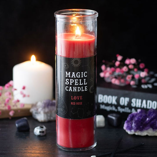 A lit Love Magic Spell candle labelled “Love: Red Rose” stands on a dark table, ideal for romantic rituals. Nearby are crystals, pink flowers, and a Book of Shadows amidst mystical décor, evoking a rose scent.