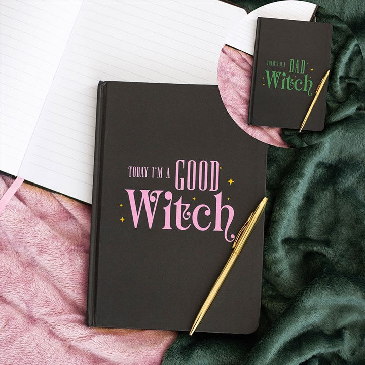 A black reversible notebook with “Today I’m a Good Witch” in pink and white, and “Today I’m a Bad Witch” in green, lies on a green blanket with a gold pen. An open notebook sits beside it. Rewritten in British English: A black reversible notebook with “Today I’m a Good Witch” in pink and white, and “Today I’m a Bad Witch” in green, lies on a green blanket with a gold pen. An open notebook lies beside it.