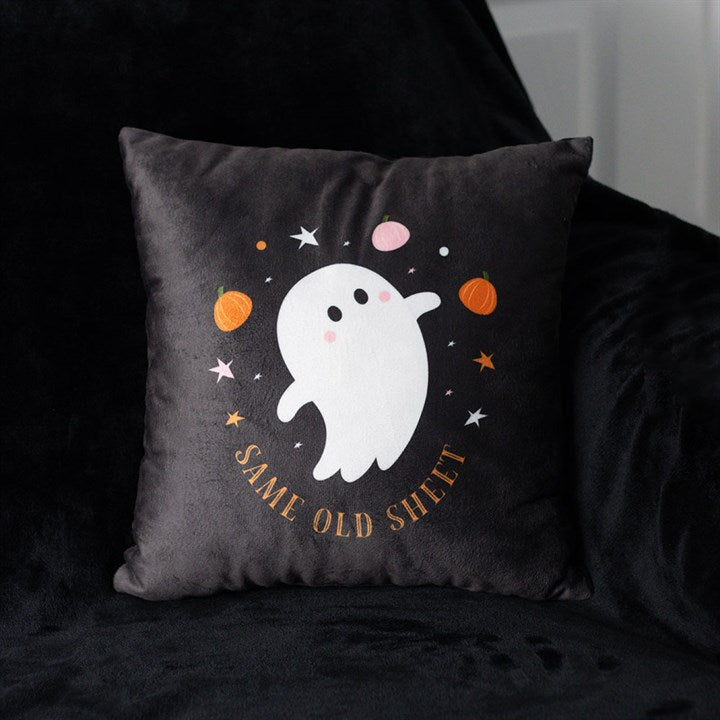 A spooky cushion for Hallowe’en décor, this black pillow features a cute white ghost with blushing cheeks, surrounded by stars, dots and pumpkins. Golden text below reads SAME OLD SHEET. The cushion rests on a dark chair.