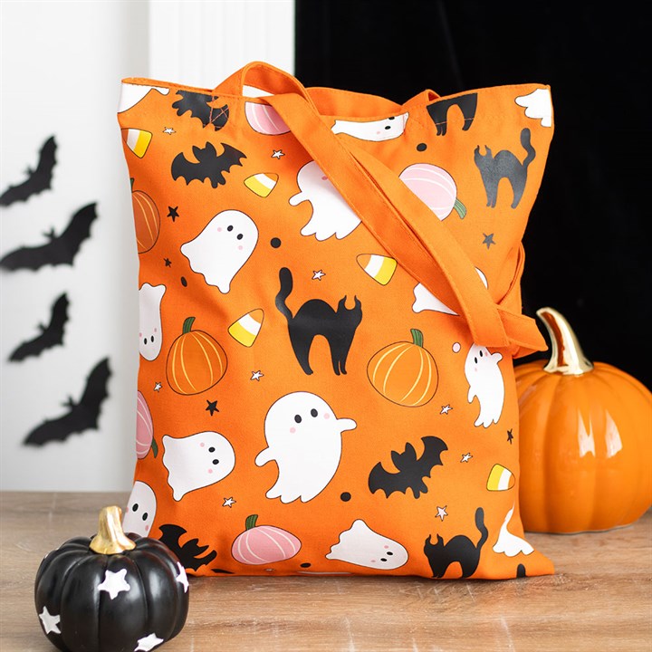 An eco-friendly trick-or-treat bag, this orange Halloween tote features ghost and pumpkin print, black cats, candy corn, and stars. It is shown with ceramic pumpkins and black paper bats for a festive touch.
