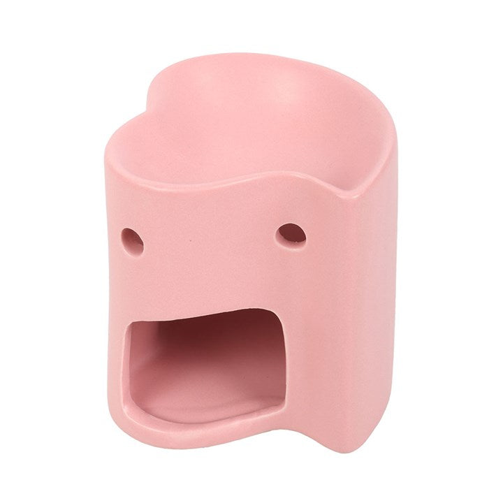 A small, pink oil burner shaped like a rounded, abstract figure with two small circular holes for eyes and a large rectangular open mouth, resembling a surprised facial expression.