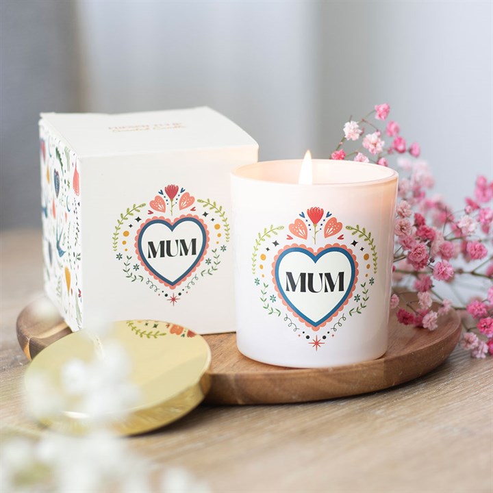 A lit white French Tulip scented candle labelled MUM in a floral heart design rests on a wooden tray with its matching box, gold lid and pink babys breath—an ideal Mother’s Day present.