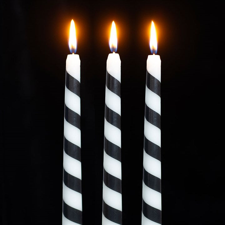 Three tall, black candy cane candles with white diagonal stripes stand side by side, each with a small, bright orange flame against a completely black background—perfect for gothic festive décor.