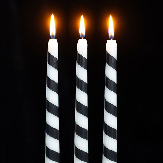 Three tall, black candy cane candles with white diagonal stripes stand side by side, each with a small, bright orange flame against a completely black background—perfect for gothic festive décor.