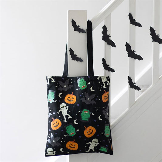 A Halloween tote bag adorned with prints of mummies, Frankenstein’s monsters, jack-o’-lanterns, bats and stars hangs on a stair rail—a perfect eco-friendly gift for Halloween enthusiasts.