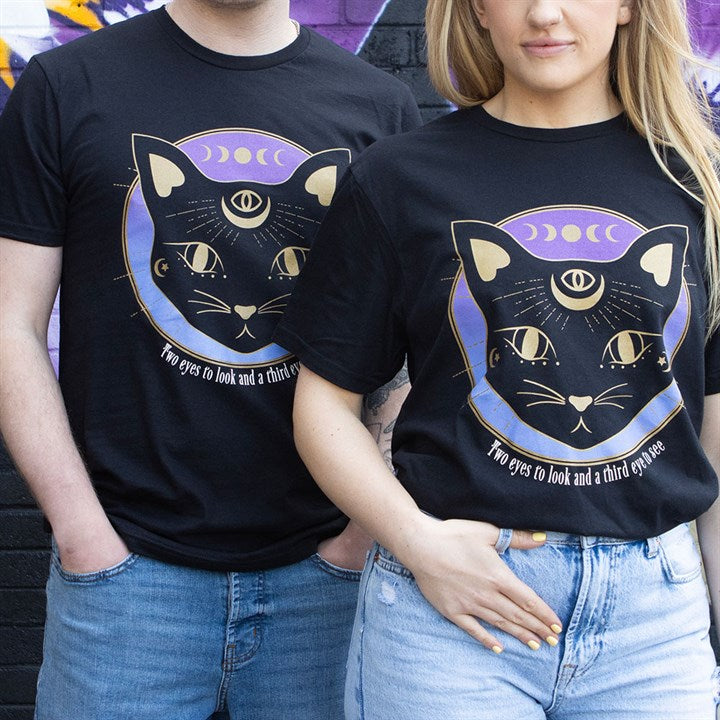 A man and a woman stand side by side wearing black T-shirts featuring the Mystic Mog black cat design, adorned with magical symbolism such as a third eye, crescent moons, and the phrase “Two eyes to look and a third eye to see.”.