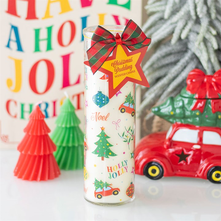 A tall white festive pillar candle adorned with prints of cars, trees, and baubles sits on a white surface. Decorated with a red tartan bow and yellow tag, it makes a perfect stocking filler amid tree figurines and a red car ornament.