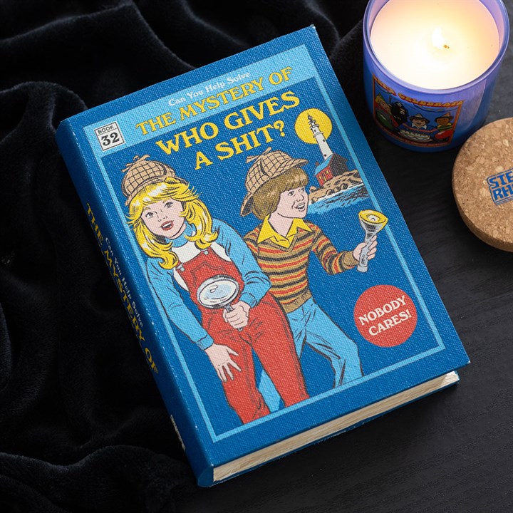 A blue book titled The Mystery of Who Gives a Shit? features illustrated children dressed as detectives with magnifying glasses. A candle labelled Steer Rohn and an MDF storage box rest on a black fabric surface.