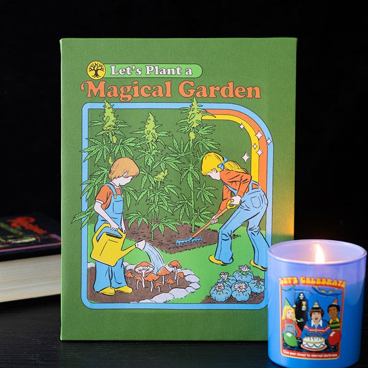 A book titled “Let’s Plant a Magical Garden” depicts two children gardening with large cannabis plants; one child waters psychedelic mushrooms while the other digs. A lit candle featuring cartoon figures sits nearby, lending retro gift charm.