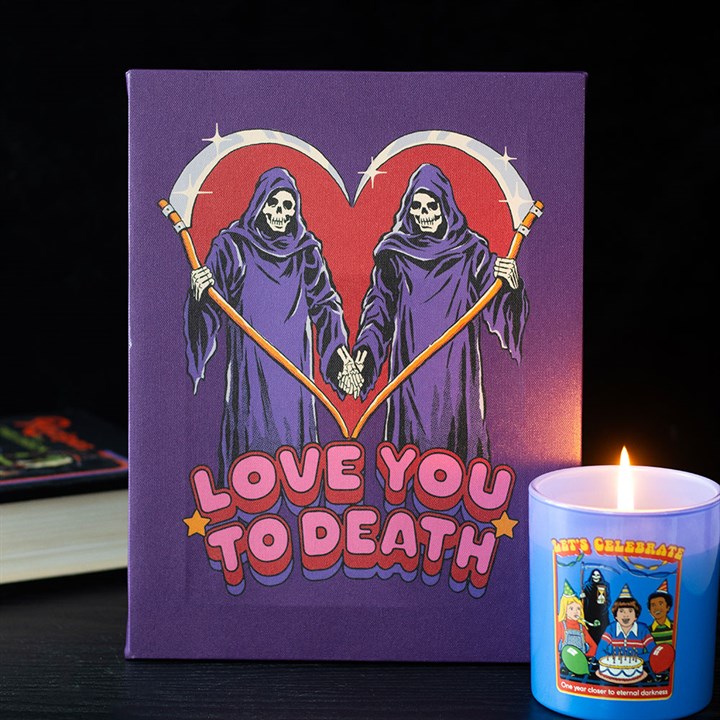 An ideal gift for a goth couple, this purple card features two Grim Reapers holding hands, their scythes forming a heart. LOVE YOU TO DEATH is boldly written underneath, with a lit candle in a cartoon mug in the foreground.