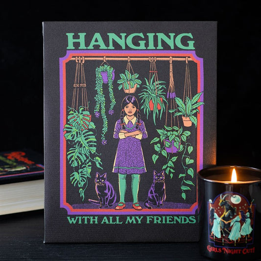 A candle burns next to a book and retro wall art depicting a girl with long dark hair among hanging and potted plants, flanked by two black cats. The text on the artwork reads: HANGING WITH ALL MY FRIENDS.
