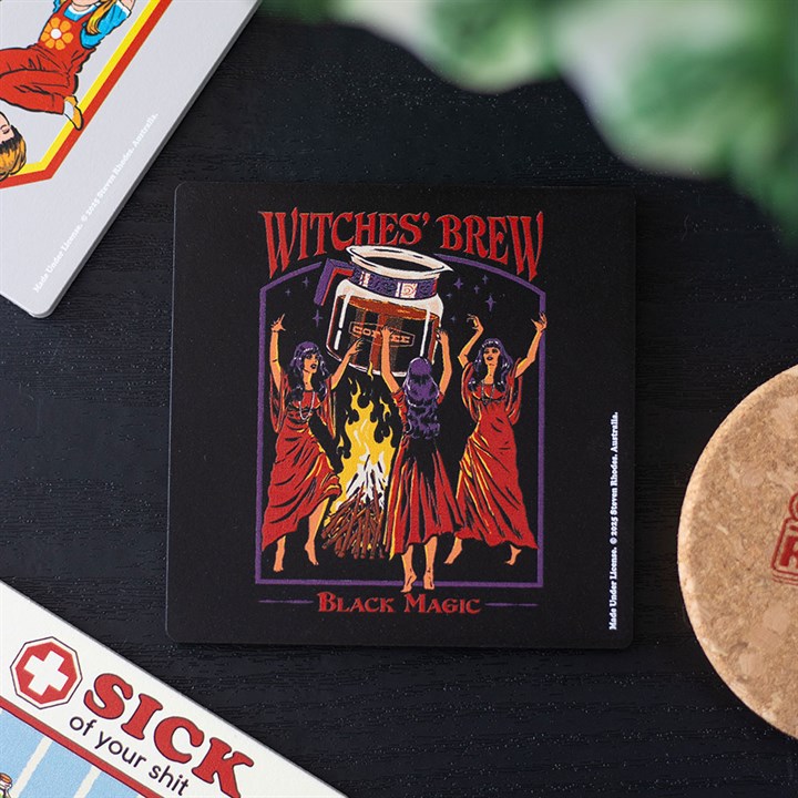 A square Steven Rhodes caffeine coaster depicts three women in red robes gathered around a cauldron over a fire, arms raised. “Witches’ Brew” and “Black Magic” are written above and below in fiery lettering. Other coasters can be seen nearby.