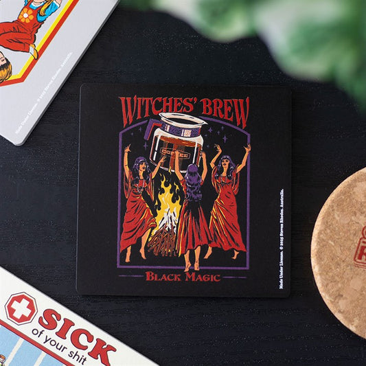 A square Steven Rhodes caffeine coaster depicts three women in red robes gathered around a cauldron over a fire, arms raised. “Witches’ Brew” and “Black Magic” are written above and below in fiery lettering. Other coasters can be seen nearby.