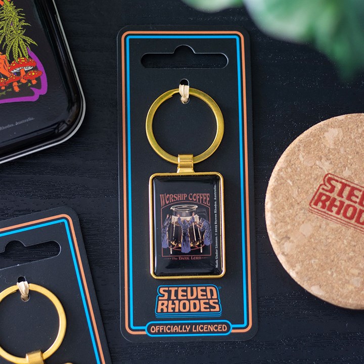 A rectangular coffee keyring featuring a “Worship Coffee” design and two coffee pots is attached to black, officially licensed Steven Rhodes packaging. Nearby are a cork coaster and part of a colourful tray—perfect for lovers of retro gifts.