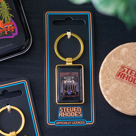 A rectangular coffee keyring featuring a “Worship Coffee” design and two coffee pots is attached to black, officially licensed Steven Rhodes packaging. Nearby are a cork coaster and part of a colourful tray—perfect for lovers of retro gifts.